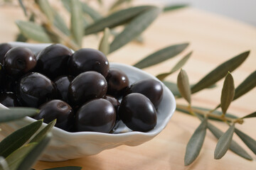 Close-up of a bowl with black olives next to some olive leaves