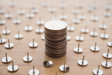 Stacked coins is in many danger thumbtacks pins on wooden table background. Financial risk assessments, losing money in investment or business venture, risk management or money fraud crime concept.