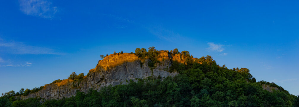 Sunlight illuminating top of rocky outcrop against blue sky; Matlock, Derbyshire, England