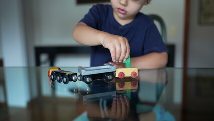 Child plays with wooden train toy at home glass table