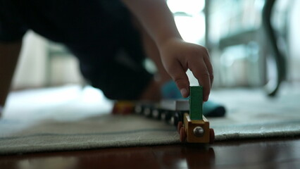 Child plays with traditional car wooden train toy on floor