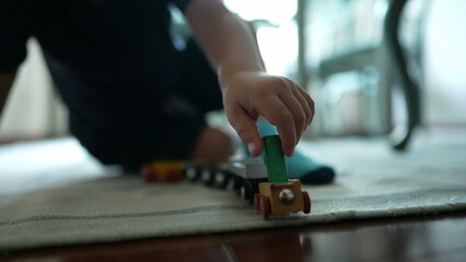 Child plays with traditional car wooden train toy on floor