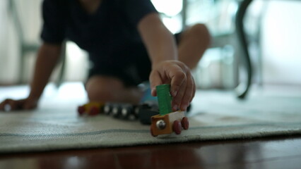 Child plays with traditional car wooden train toy on floor