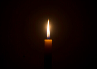 A single burning candle flame or light glowing on an orange candle on black or dark background on...