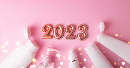 Top view of the cosmetics containers on pink background.Rose gold numbers 2023 above with shiny bokeh.