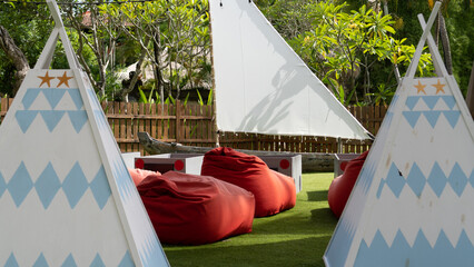 several beanbag chairs, small tent, and rectangular boxes placed on outdoor children playing area 