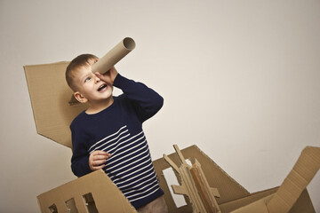 child plays with a cardboard boat and a tube as a spyglass