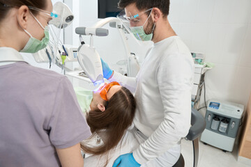 Naklejka na ściany i meble Experienced dentist doing dental procedure on client with modern equipment