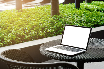 Laptop with blank screen for creative design on the table nearby garden  with sun ray effect. Computer notebook with monitor clipping path for present landing page. Laptop computer mock up template.