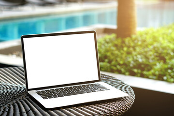 Laptop with blank screen for creative design on the table nearby pool with sun ray effect. Computer notebook with monitor clipping path for present landing page. Laptop computer mock up template