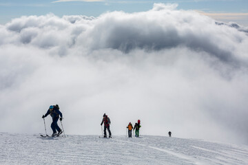 hikers with backpacks are on a high snow-covered peak above the clouds in the mountains. success achievement on the edge