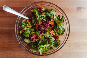 healthy winter salad with red beetroot, carrot arugula and green salad in glass bowl on wooden table