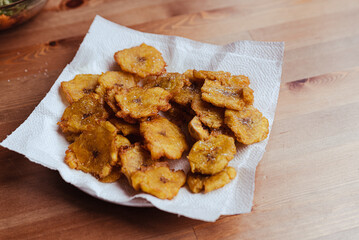 Fried slices of ripe plantains chips , traditional and popular snack and side dish in Central America and South America, photographed overhead on slate with natural light on wood table with copy space