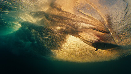 Surfer rides the wave and grabs the water surface. Underwater through the wave view of the surfer...