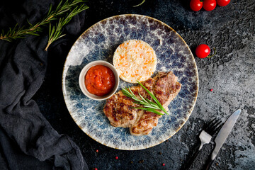 Pork steak with rice and tomato sauce on plate on dark table top view