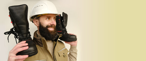 young bearded man, builder in uniform, hard helmet holds in hands and inspects black work leather...