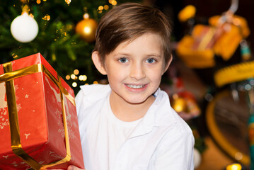 Fototapeta na wymiar little smiling boy holding a box with a gift, opens presents at christmas