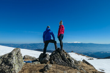 Couple with panoramic view of mountain hut Wolfsbergerhuette (Wolfsberger Huette) on Saualpe, Lavanttal Alps, Carinthia, Austria, Europe. Looking at snow covered Koralpe. Alpine road to remote cottage