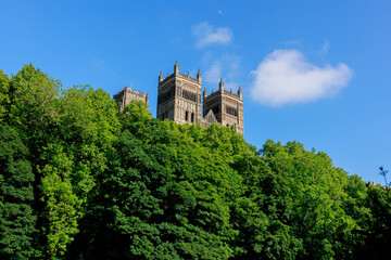 Fototapeta na wymiar Durham England: 2022-06-07: Durham Cathedral exterior during sunny summer day with lush green trees and blue sky. Closeup view