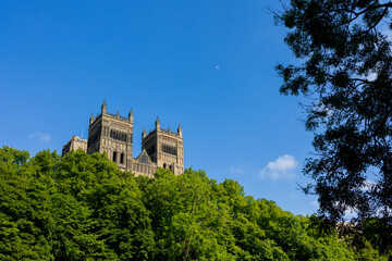 Fototapeta na wymiar Durham England: 2022-06-07: Durham Cathedral exterior during sunny summer day with lush green trees and blue sky. Closeup view