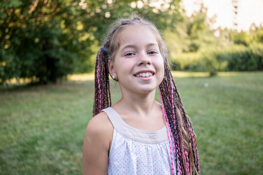 a girl with dark eyes with braided Afro braids walks in the park. A child walks in a summer green park. Fun holidays. The girl smiles and laughs. Happy childhood