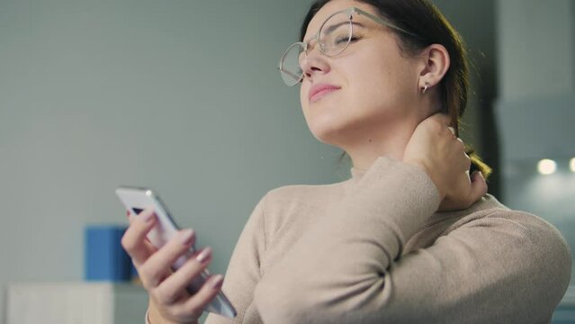 Brunette woman in eyeglasses frowning in pain massaging sore neck, feeling pain and numbness, looking for symptoms on internet, booking for mri, risk of hernias and protrusions in the cervical spine