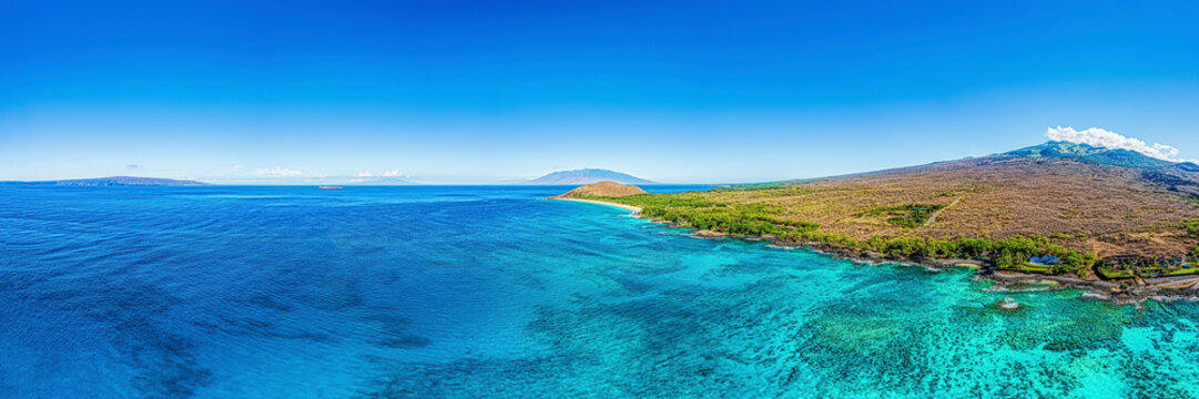 Aerial view of the turquoise water of the Pacific Ocean surrounding the volcanic islands of the Hawaiian Islands with a vibrant blue sky; Maui, Hawaii, United States of America