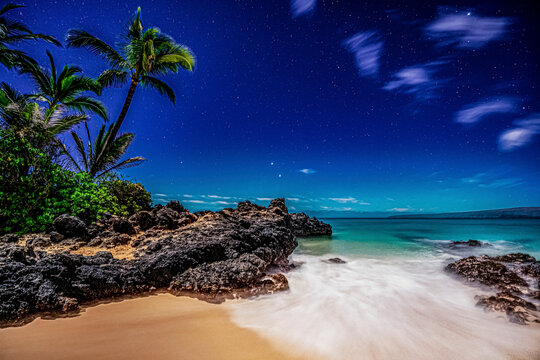 Starry skies viewed from a beach with palm trees and surf rolling into golden sand at Makena Cove on the island of Maui, Hawaii, USA; Maui, Hawaii, United States of America