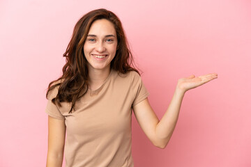 Young caucasian woman isolated on pink background holding copyspace imaginary on the palm to insert an ad