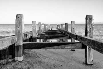Abstract view of wooden sea groynes located at a popular beach. Warning signs about current dangers can be seen in the distant as are gulls.