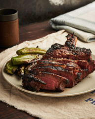Grilled T-bone steak with charred okra on a ceramic plate.