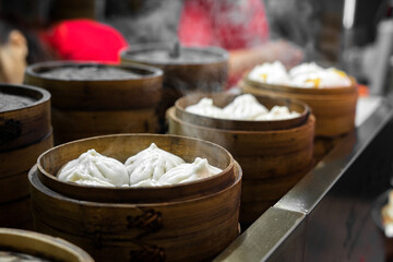 Steaming bamboo baskets of xiao long bao (soup dumplings) in a row, with focus on the closest;...
