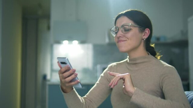 Positive young woman in big stylish eyeglasses enjoying favourite music playing in music application on her smartphone, dancing, moving to the rhythm, good mood, aspiration