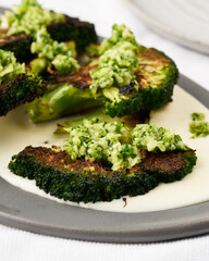 Charred broccoli steaks with herb sauce on a cream plate.