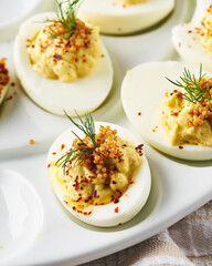 Deviled eggs garnished with paprika and dill on a white plate.