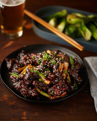 General Tso's chicken with scallions, sesame seeds on a black plate.