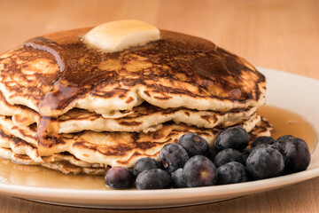 Golden pancakes topped with butter, dripping with maple syrup, accompanied by fresh blueberries.