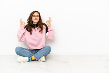 Young caucasian woman sitting on the floor isolated on white background in zen pose