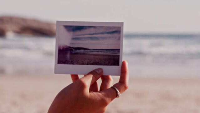 Beach, travel and photograph with a the hand of a woman outdoor on the sand by the ocean during summer. Sea, nature and polaroid with a female holding a picture while on holiday or vacation