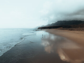 Drone photo of a man in the middle of the beach alone with the mountains in the background