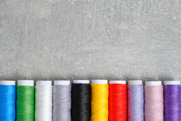 Reels with multi colored sewing threads gray concrete background.