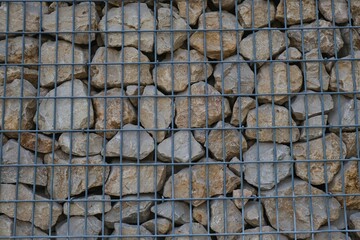 Weather-resistant and rust-proof gabion wall, welded mesh and rock- stones landscaped garden fence. Stone Basket Cage background. Wirework container filled with boulders,used as retaining walls.