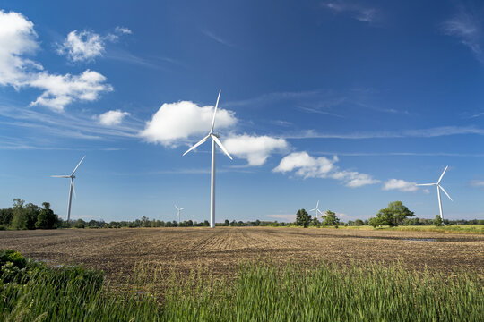 Large metal wind mills in a farm field with blue sky and clouds, West of Port Colborne; Ontario, Canada