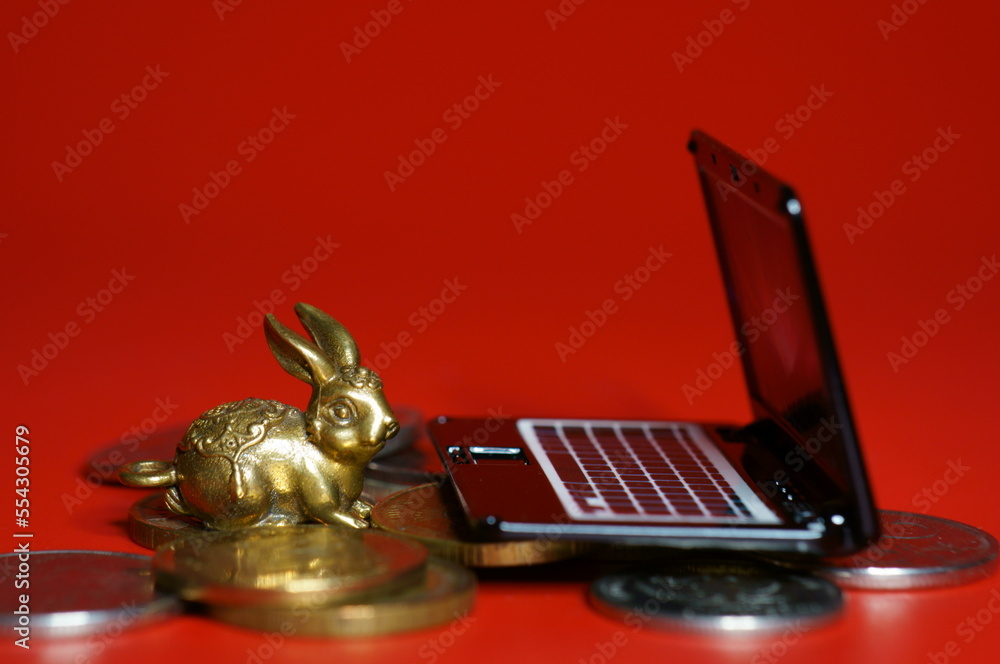 Canvas Prints A rabbit figurine with coins and a laptop on a red background. Financial symbol. Business strategies.