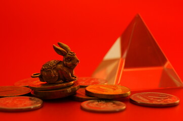 Rabbit figurine with coins on a red background. Financial symbol. The year of the rabbit.