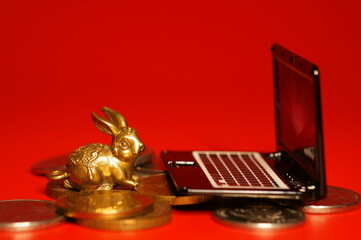 A rabbit figurine with coins and a laptop on a red background. Financial symbol. Business...