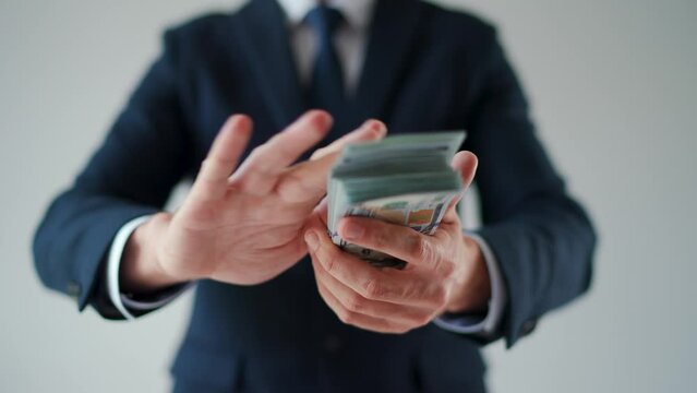 Formally dressed man makes money rain from US dollar bills. Slow motion.