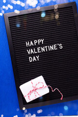 St. Valentines day postcard. Letterboard with congratulation phrase  and box with present oh bright blue paper textured background. Top view. Bokeh light. - 554314253