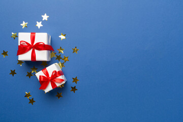 Fototapeta premium Gift box and stars confetti on color background, top view
