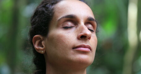 Woman meditating outdoors, taking a deep breath with eyes closed - obrazy, fototapety, plakaty